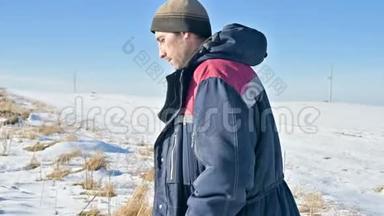 一幅画，描绘了一个穿着<strong>帽</strong>子和<strong>保暖</strong>夹克的沉思的人在阳光明媚的冬天在一下雪的户外田野里的特写